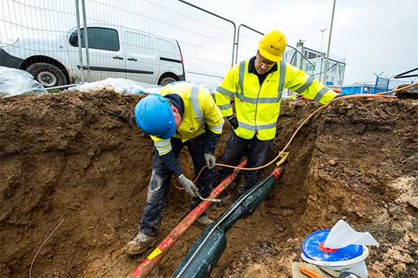 2 engineers in an excavation using blow torch to shrink a cable joint