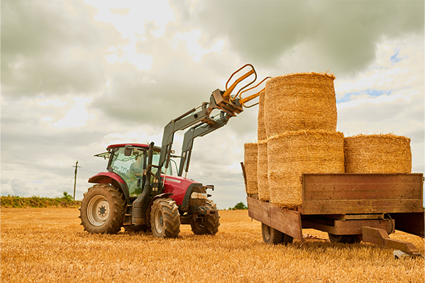 Image of tractor using extendable arm to remove haybale from lorry at height 